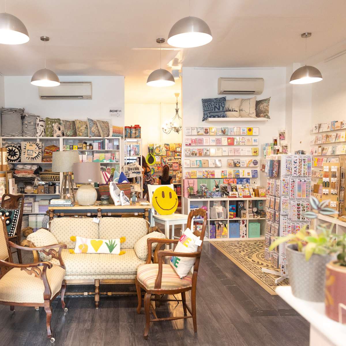A quaint retail shop filled with various items, including cards, stationery, and decorative furnishings, arranged around seating areas.