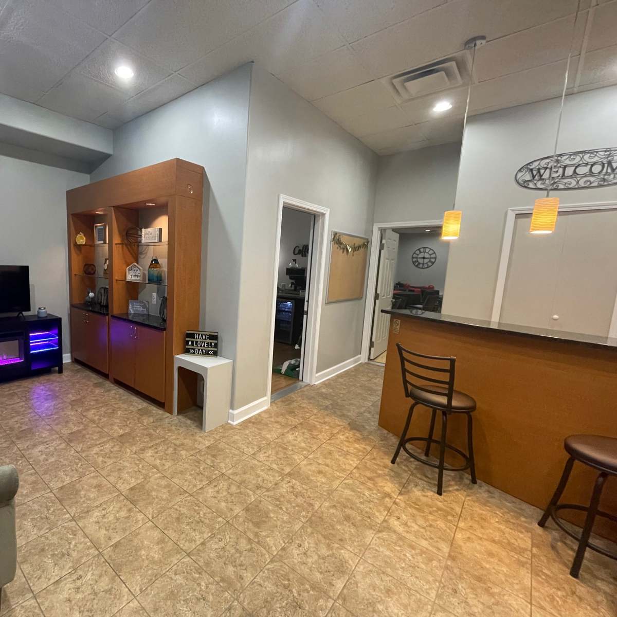 A modern interior space featuring a sitting area with two chairs, a television, a display unit, and a bar counter with two stools.