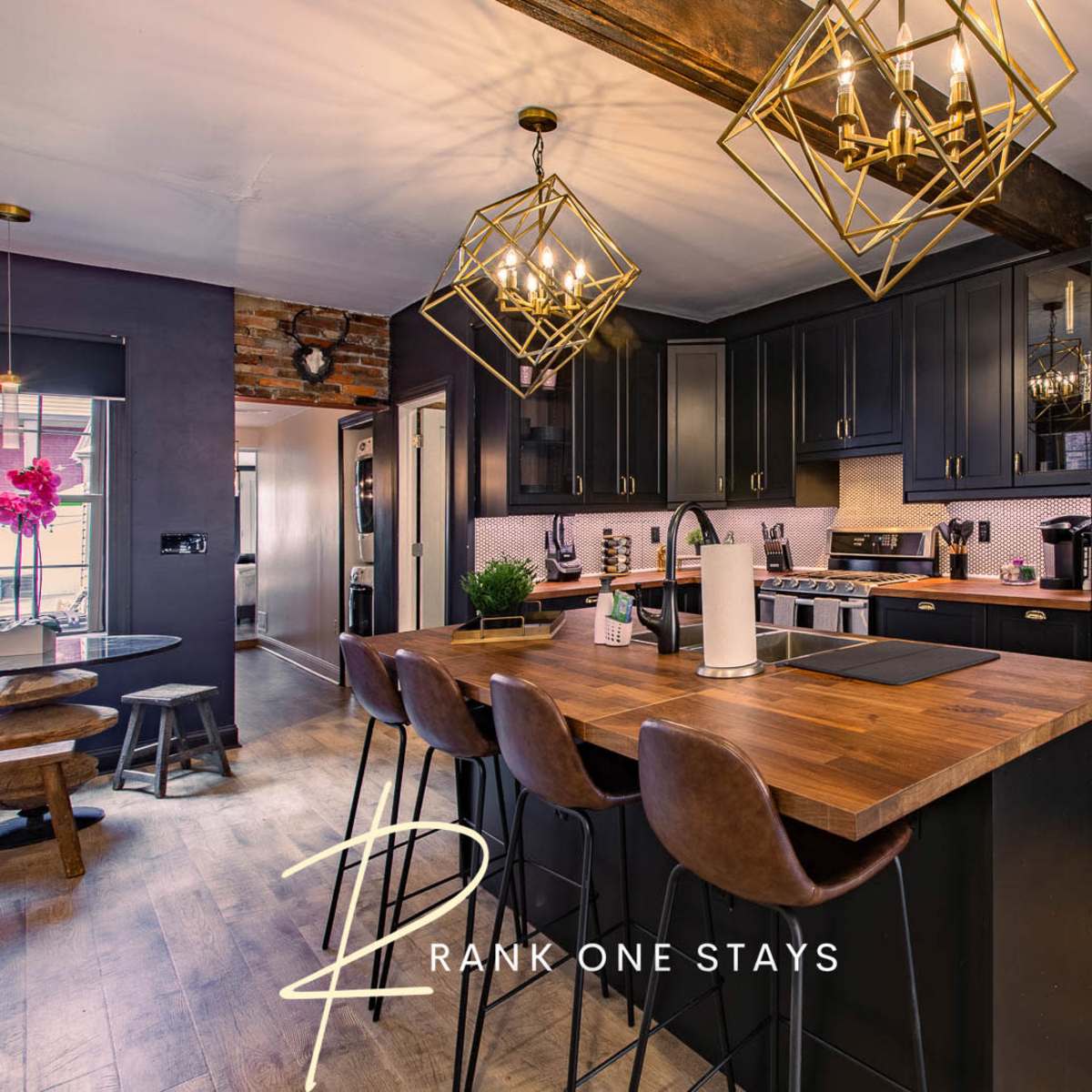 A modern kitchen with dark cabinetry, a wooden countertop, and gold pendant lights above a bar seating area.