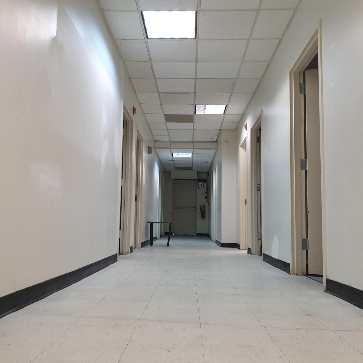 A long, narrow hallway with contrasting light and dark walls features several doorways on either side and exits at both ends.
