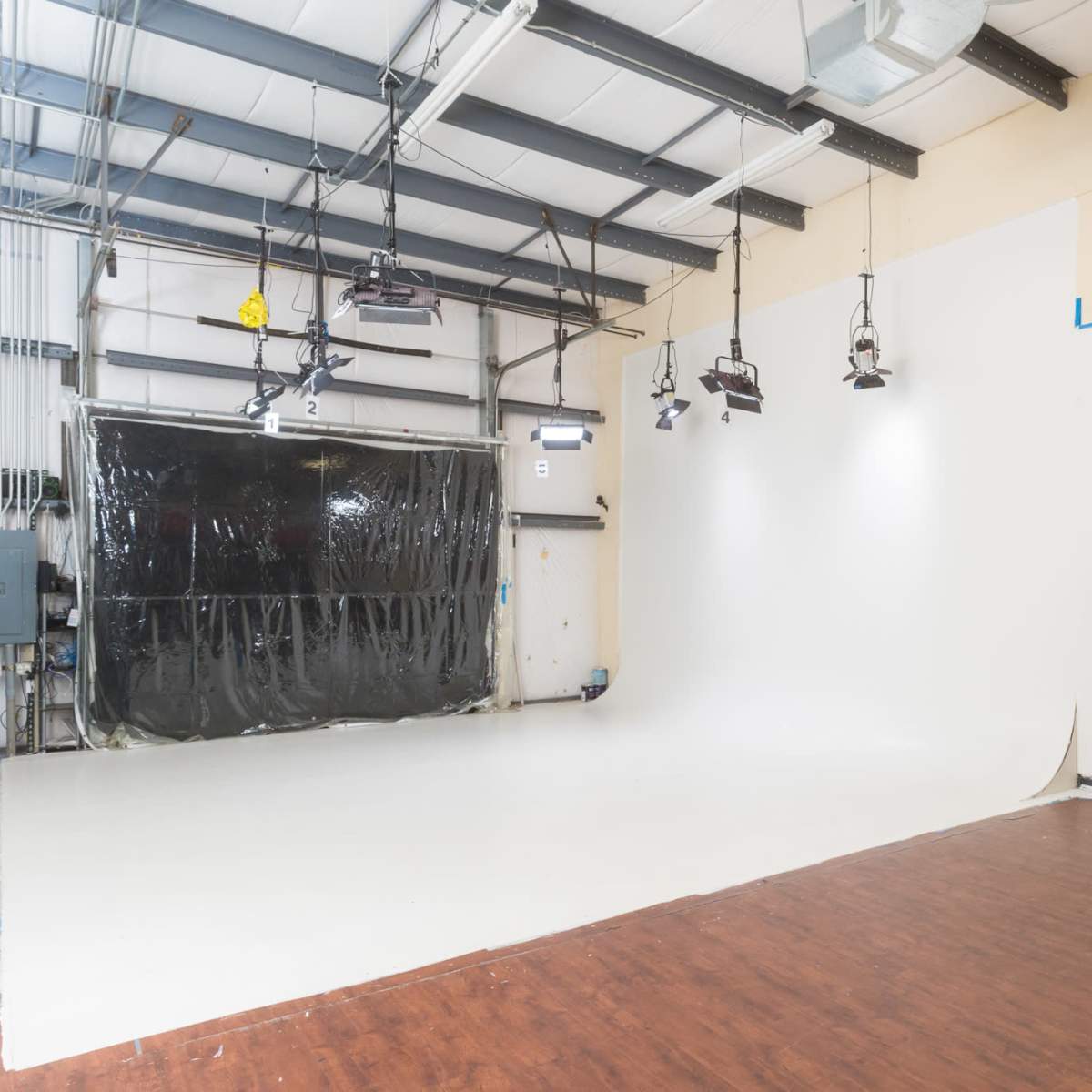 A photography studio with a large white backdrop, wooden flooring, and overhead lighting equipment.