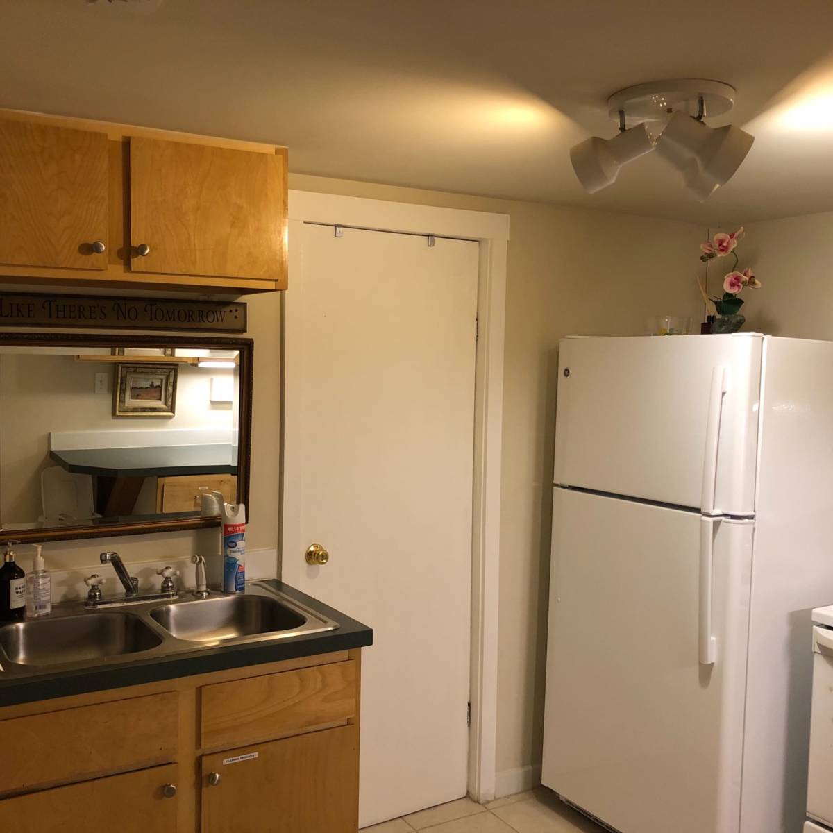 A small kitchen with wooden cabinets, a white refrigerator, a stove, and a mirror on the wall.