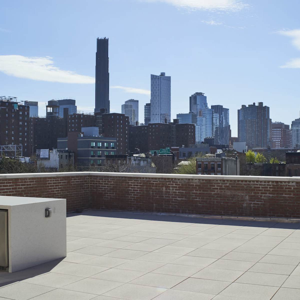A rooftop terrace features a modern outdoor kitchen and offers a view of a city skyline with tall buildings under a clear blue sky.