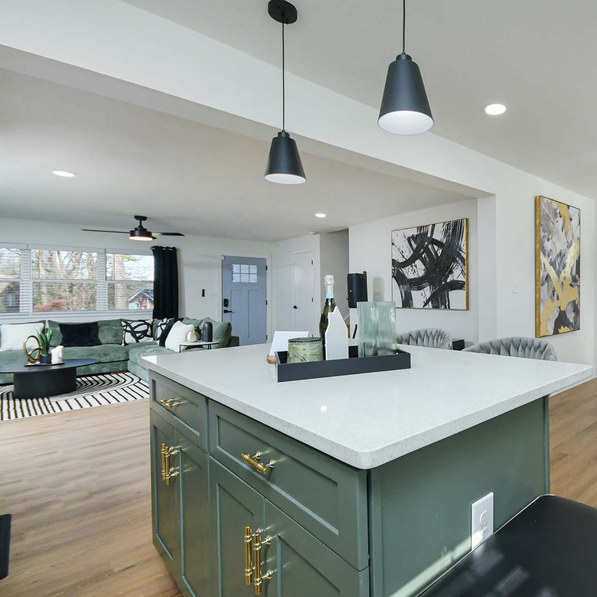 A modern open-concept living area features a kitchen island with a white countertop, green cabinetry, and dining and lounge spaces adorned with contemporary decor.