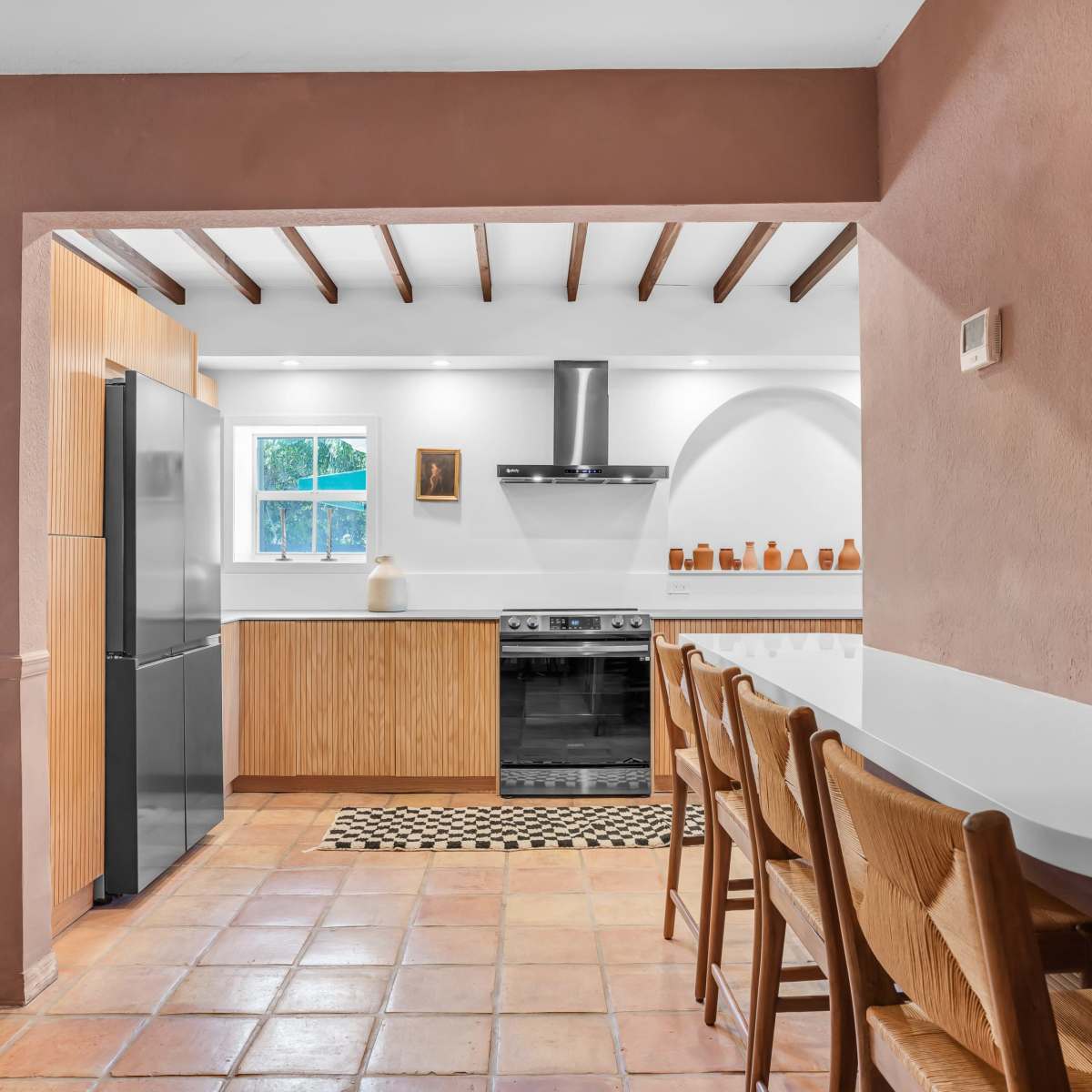 A modern kitchen features wooden cabinetry, a stainless steel oven, and a tiled floor, with a breakfast bar and seating area.