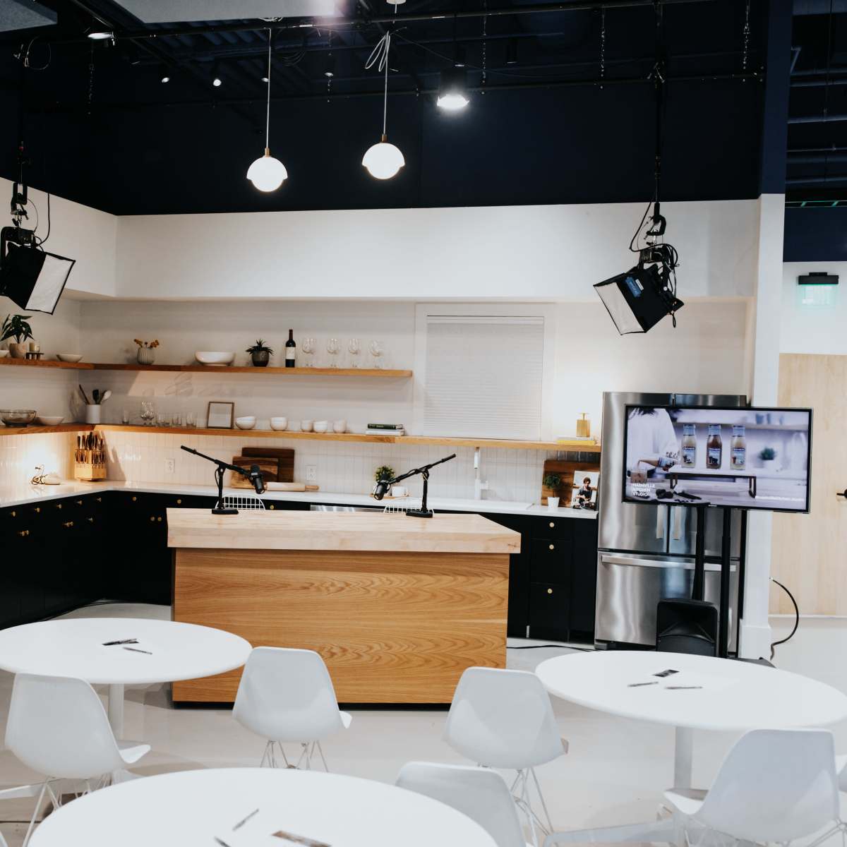 A man adjusts lighting equipment in a modern kitchen studio setup with cameras and tables arranged for filming.