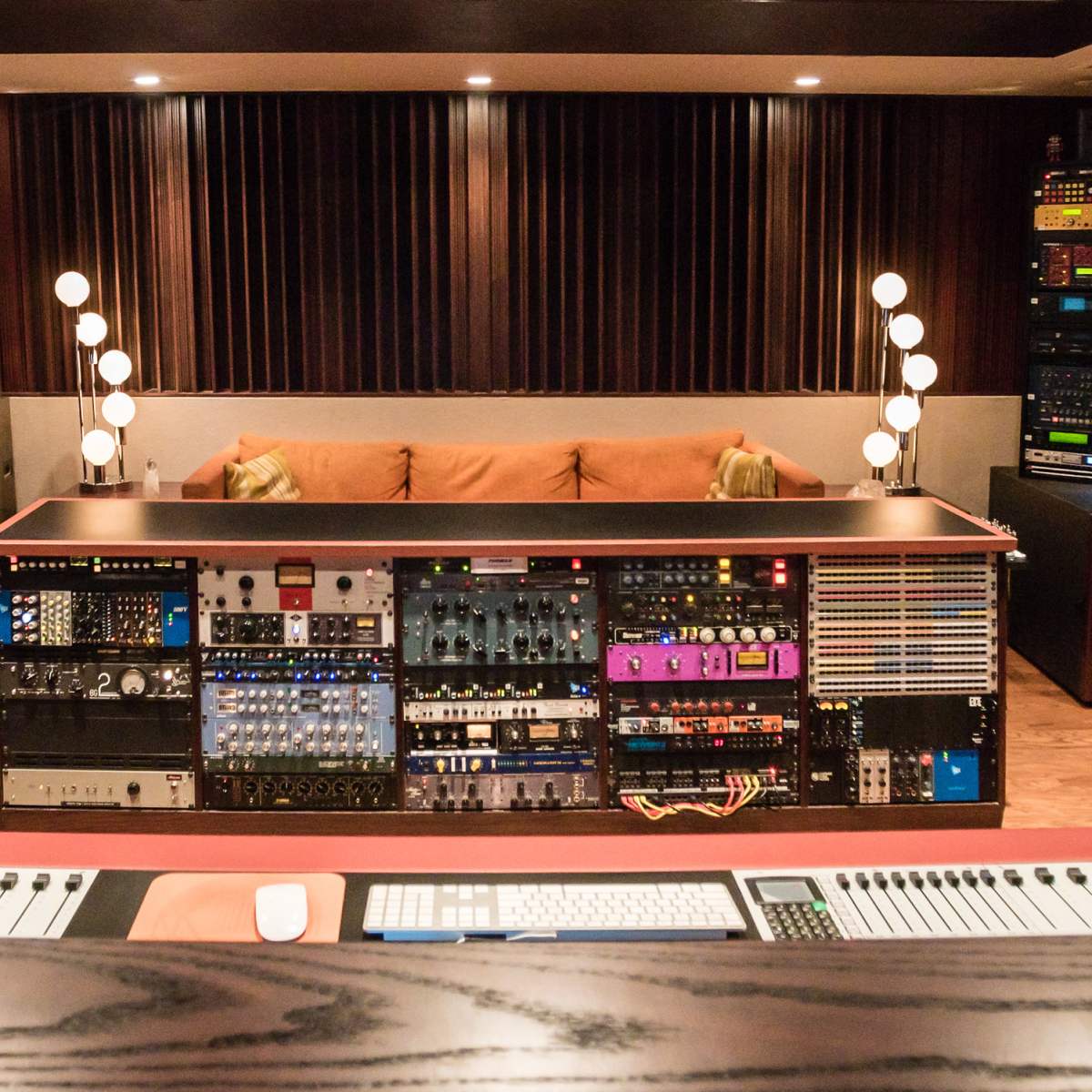 A music studio featuring an array of audio equipment, a central mixing console, and multiple guitars arranged along the walls.