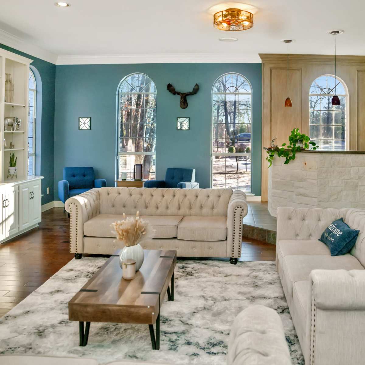 A spacious living room features two tufted sofas facing a wooden coffee table, with a stone fireplace and a bar area in the background.