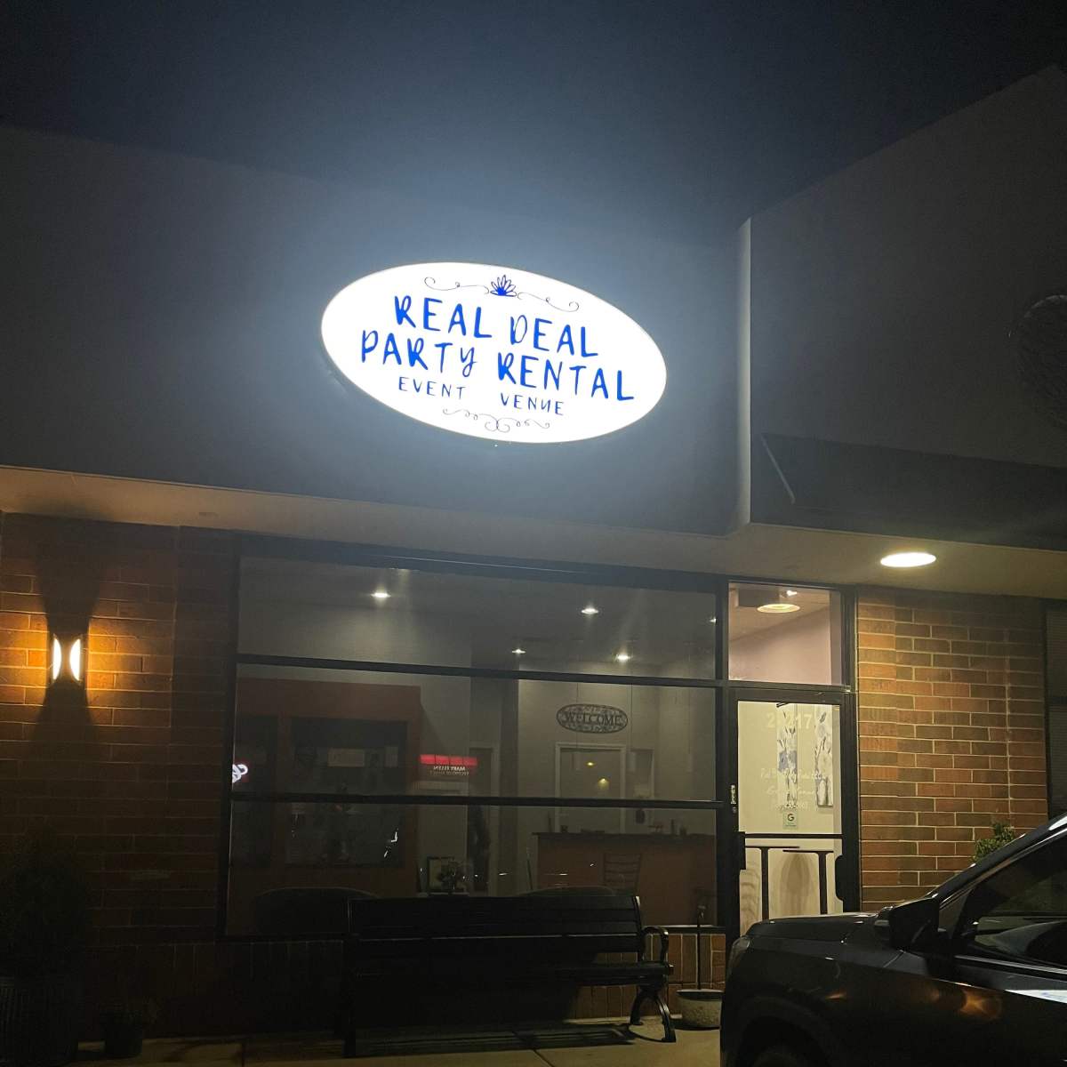 A dimly lit storefront with a sign reading "Real Deal Party Rental" displayed above the entrance.