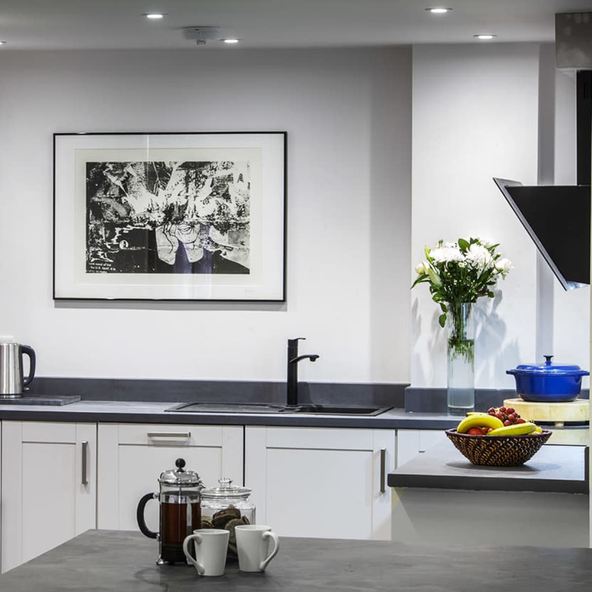 A modern kitchen with white cabinets, a black refrigerator, a countertop, a sink, and a variety of appliances including a coffee maker and a fruit bowl.