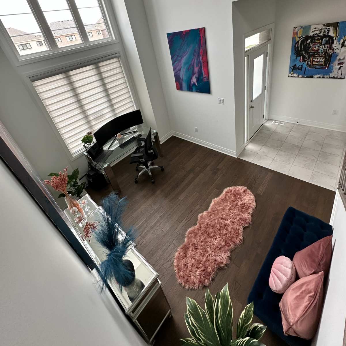 A bright, airy room with large windows, featuring a desk and chair, a plush rug, and colorful artwork on the walls.