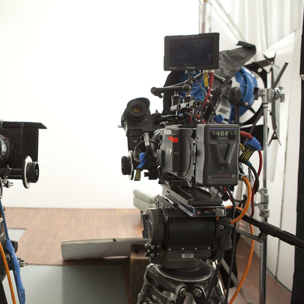 Two video cameras on tripods are positioned facing a plain white backdrop in a studio setup.