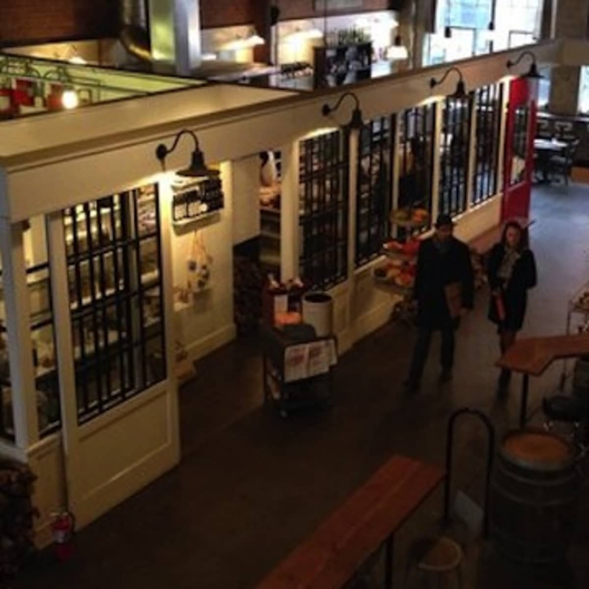 A bustling indoor market with wooden tables, various stalls, and large windows letting in natural light.