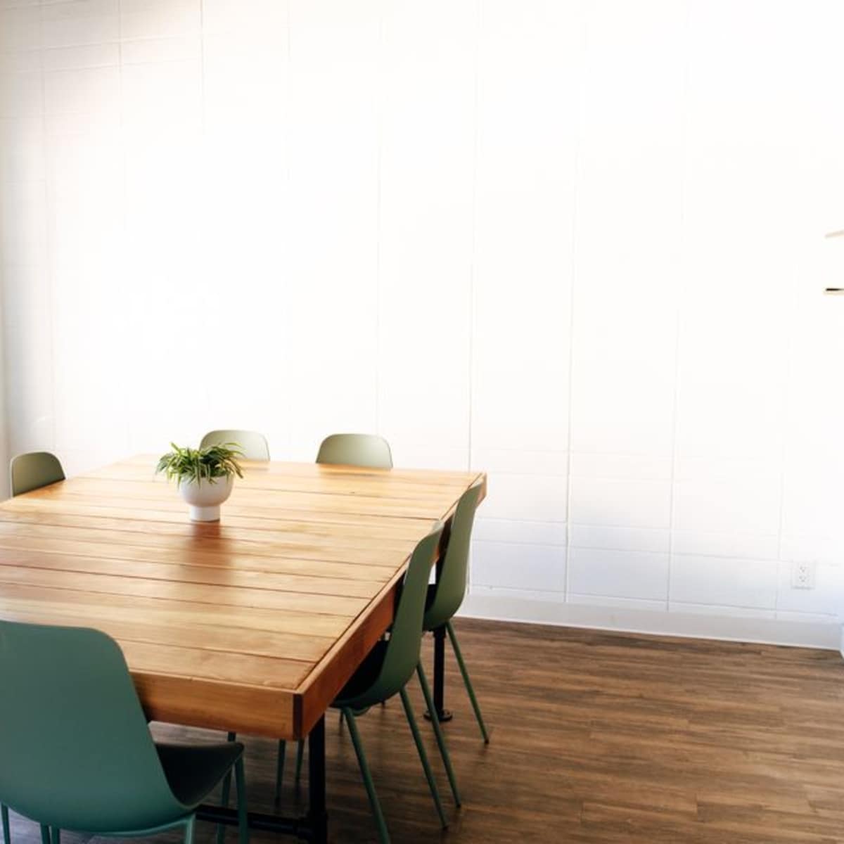 A minimalist meeting room with a wooden table surrounded by green chairs and a small plant in the center.