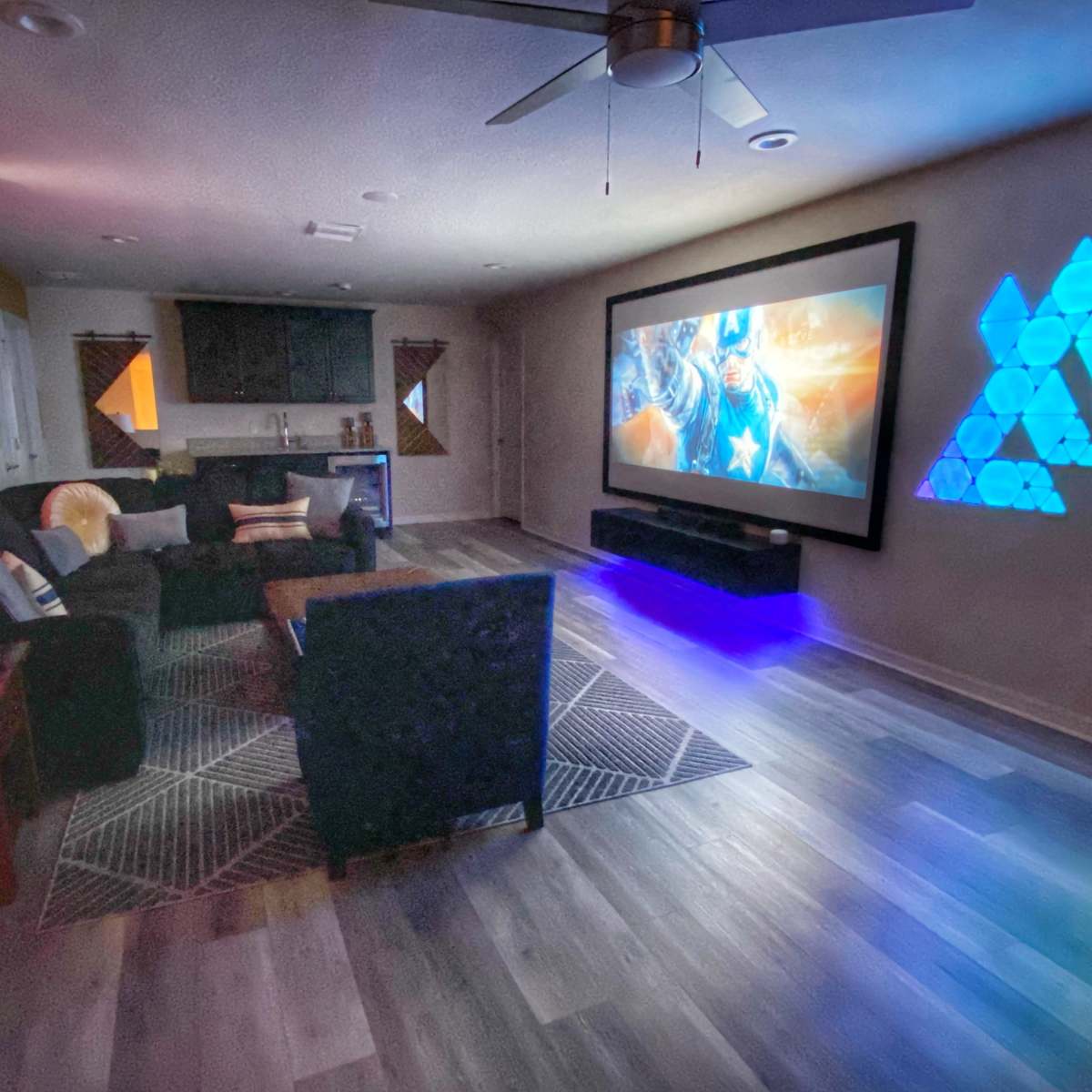 A modern living room with a large projection screen displaying a superhero theme, accompanied by colorful lighting accents and a cozy seating area.