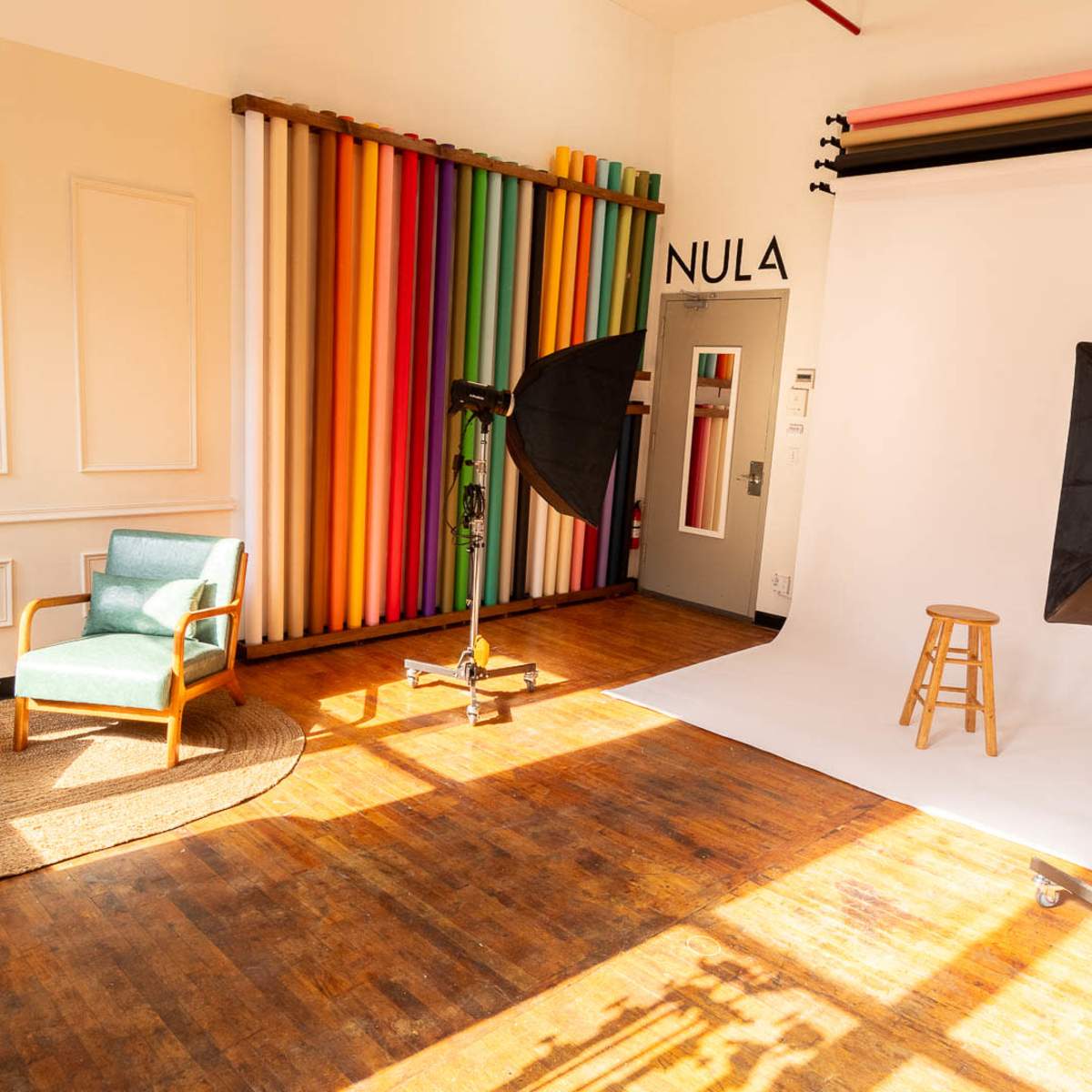 A photography studio with a colorful backdrop, two softbox lights, a stool on a white backdrop, and a pair of chairs nearby.