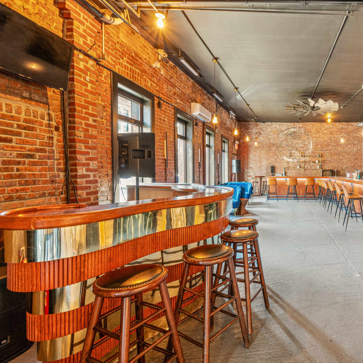 The interior of a bar features exposed brick walls, wooden furniture, and pendant lighting, with a curved wooden bar in the foreground.