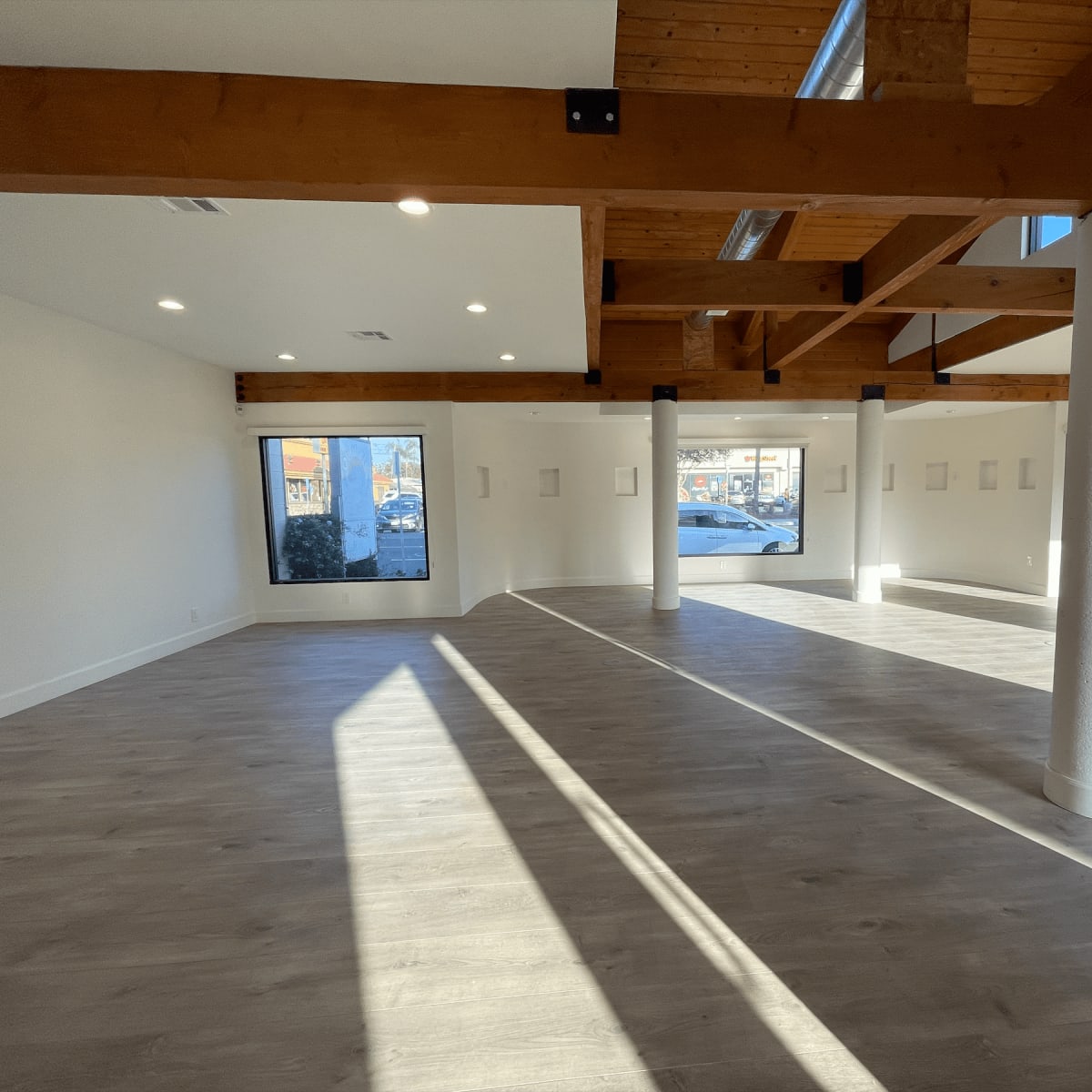 An empty interior space with wooden beams, large windows, and light-colored flooring.