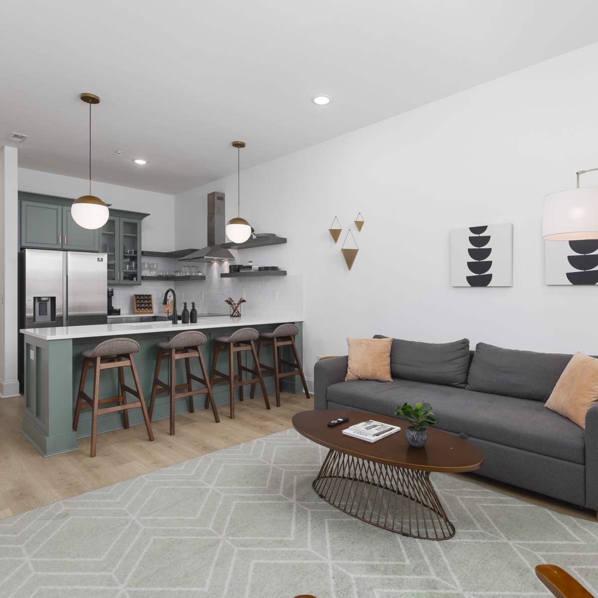 A modern living room with a gray couch, a wooden coffee table, and a kitchen area featuring bar stools and green cabinetry.