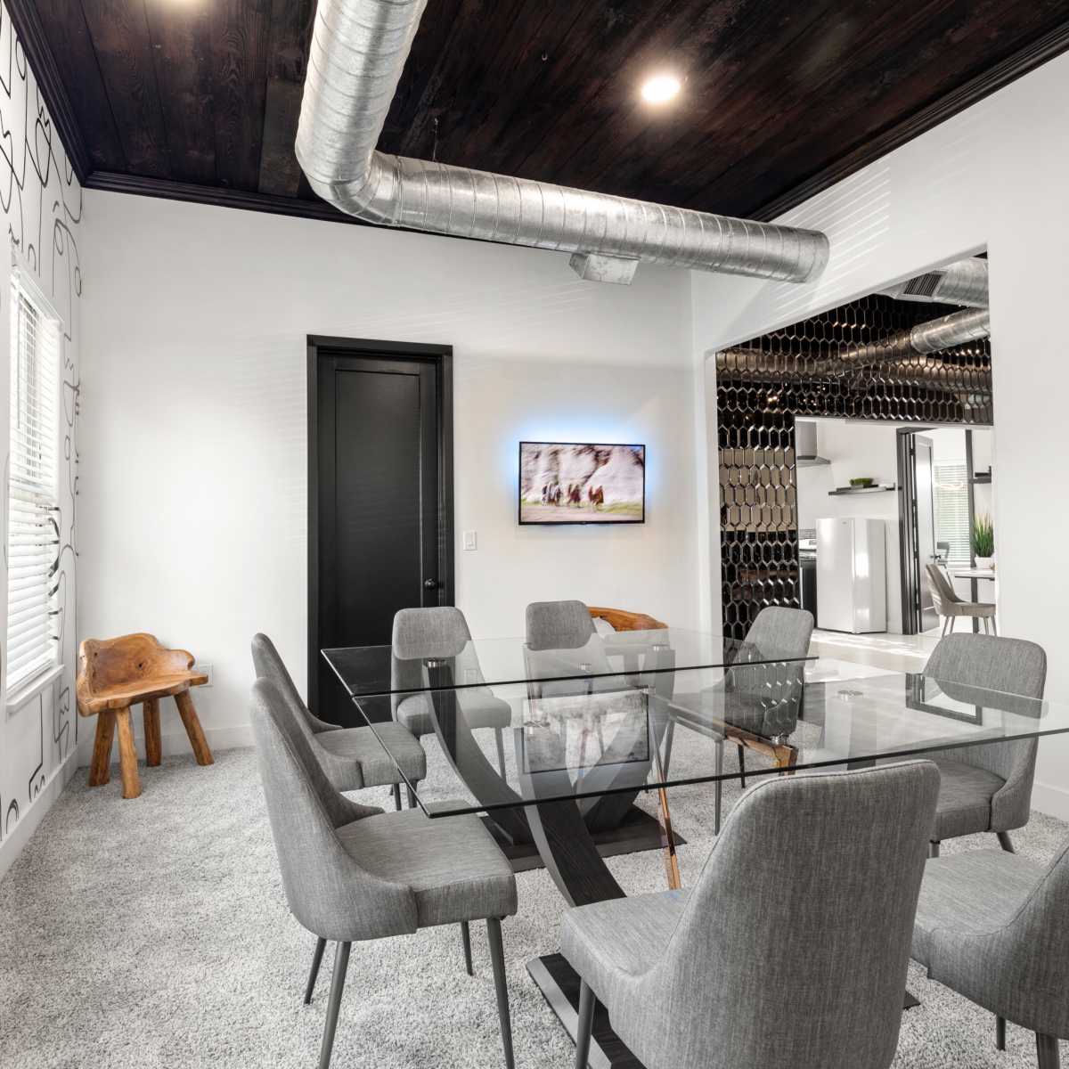 A modern conference room features a glass table surrounded by gray chairs, with a wall adorned with abstract line art and a TV mounted in the corner.