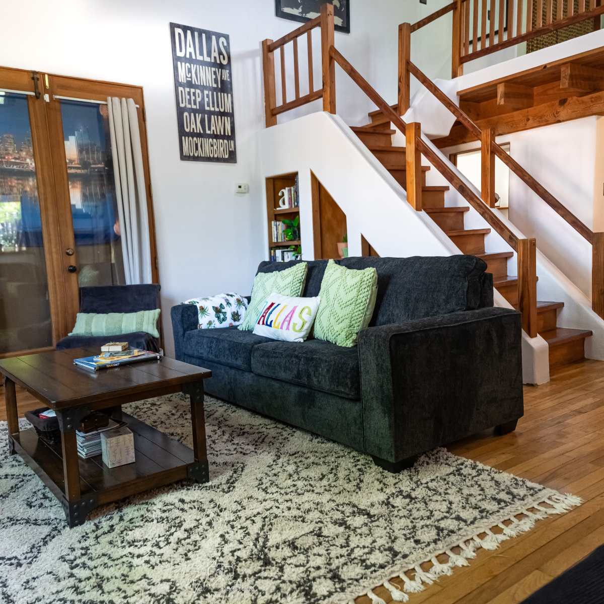 The living room features a dark blue couch with decorative pillows, a wooden coffee table, a patterned area rug, and a staircase leading to an upper level.
