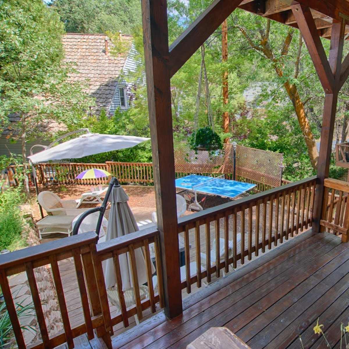 A wooden deck overlooking a backyard with outdoor furniture, a patio umbrella, and a blue pool.