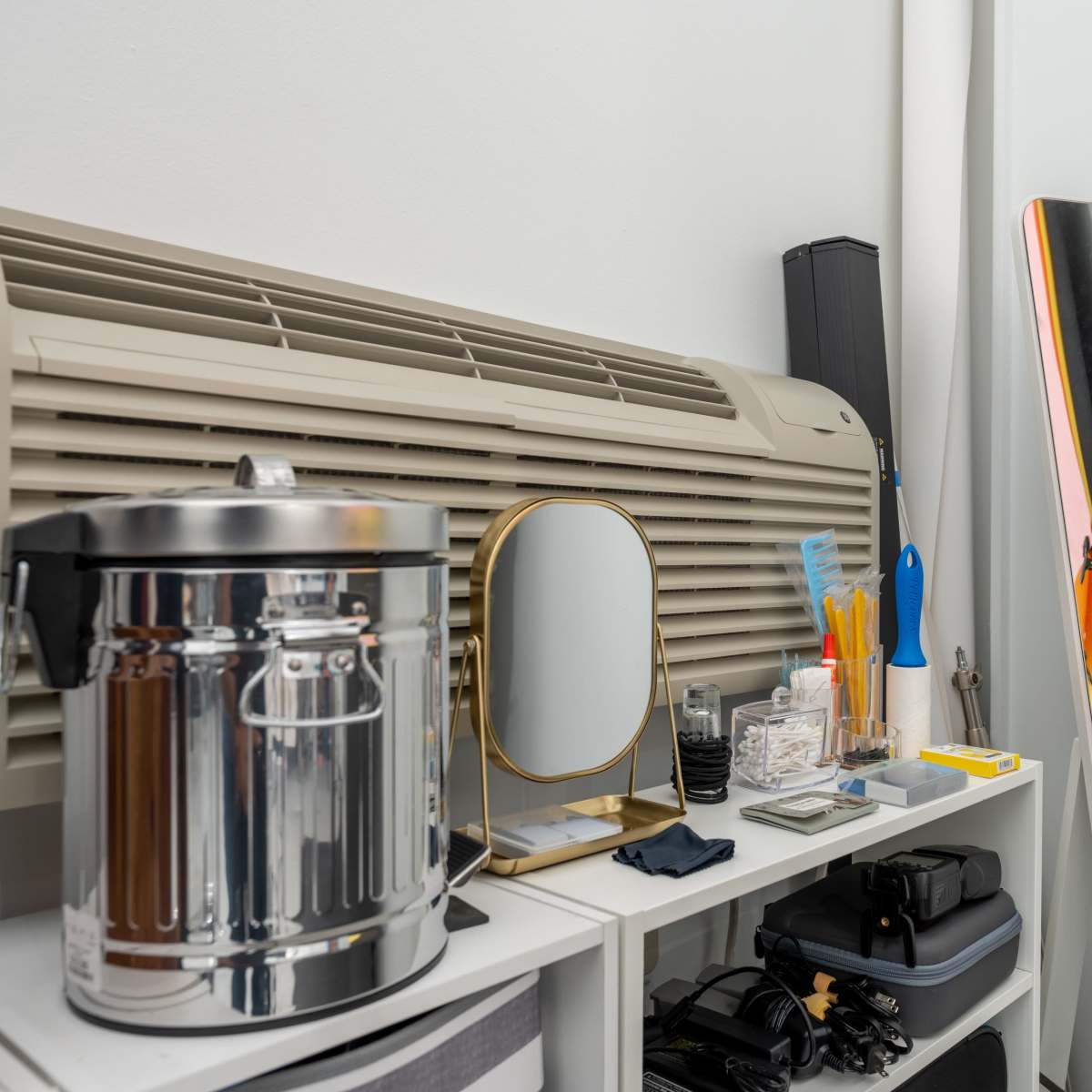 A collection of organizational items, including a mirror, a metal container, and various tools, is arranged on a shelf beside an air conditioning unit.