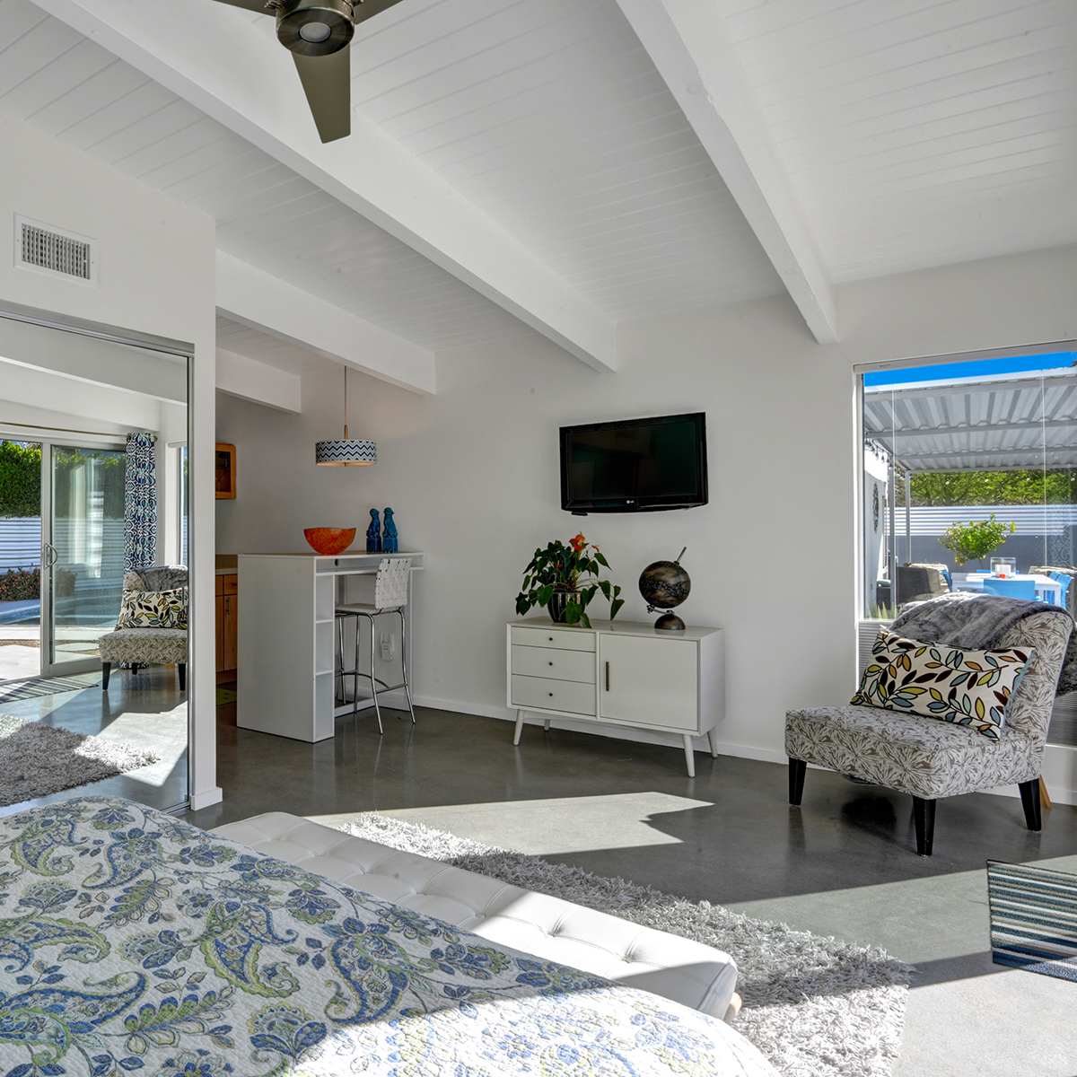A bright bedroom with a large mirror, modern furniture, and sliding glass doors leading to an outdoor space.
