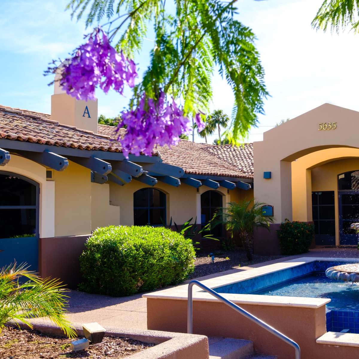 A building with a fountain surrounded by lush landscaping and blooming flowers.