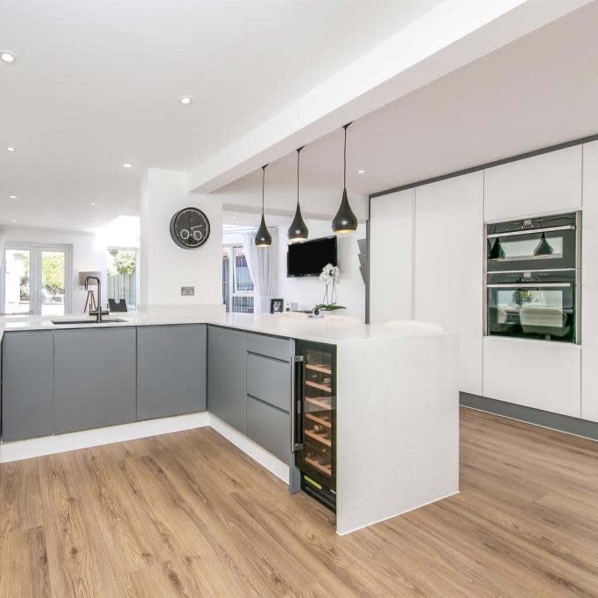 A modern kitchen with gray cabinetry, a white countertop, and wooden flooring, featuring built-in appliances and pendant lighting.