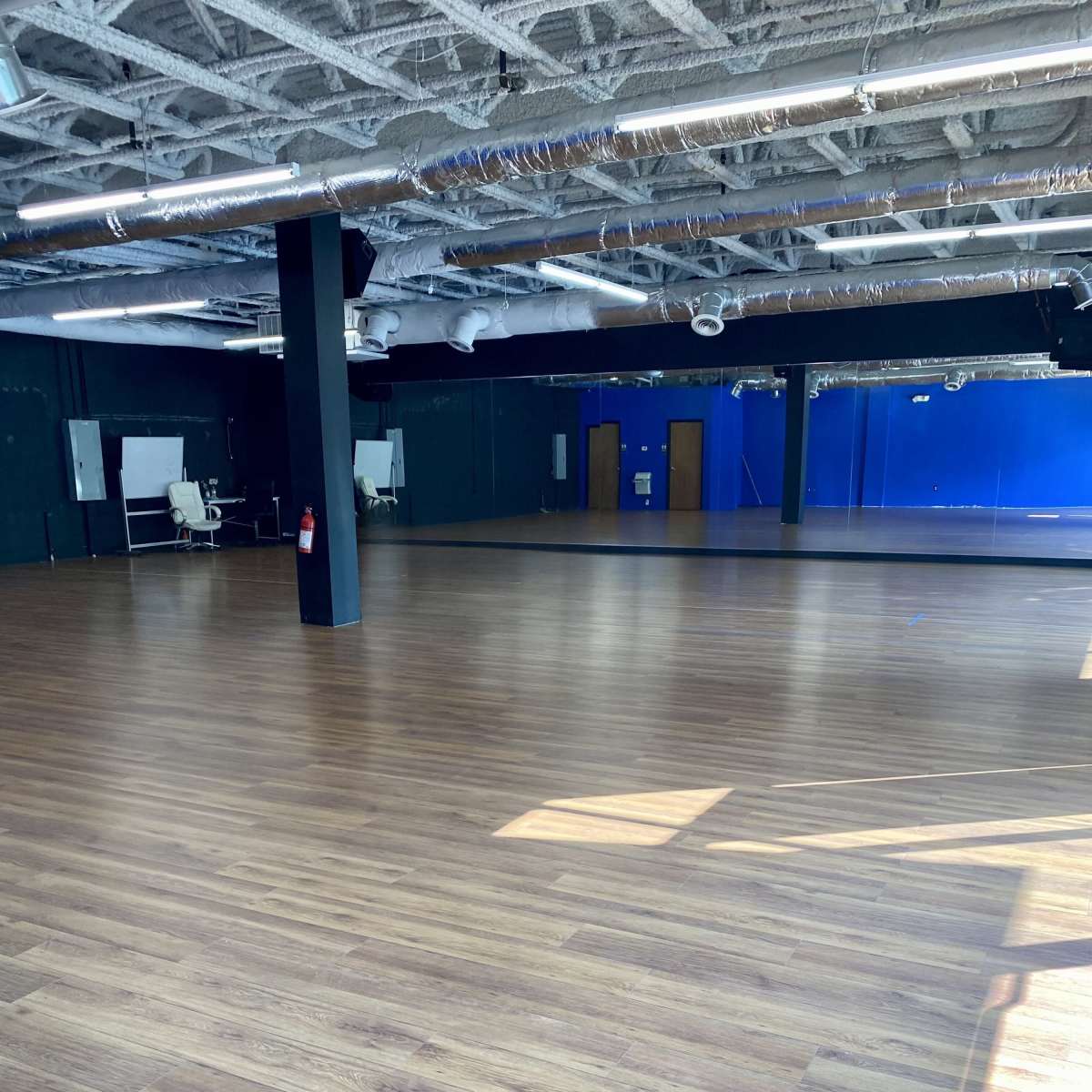 An empty room with a wooden floor, large windows, and mirrored walls.