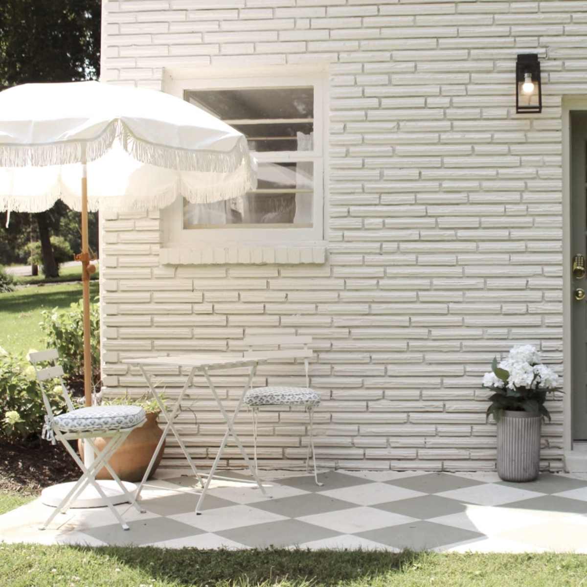 A light-colored brick house entrance with a decorative door, a small table and chairs, and a white patio umbrella.