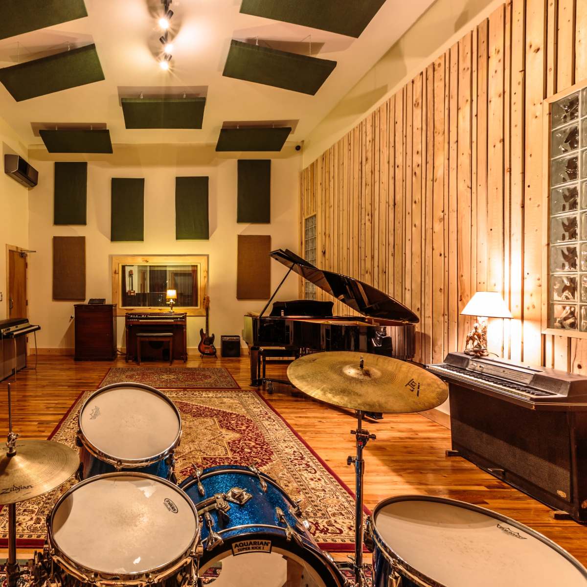 A soundproofed music studio featuring a drum set, a grand piano, various instruments, and acoustic panels on the walls and ceiling.