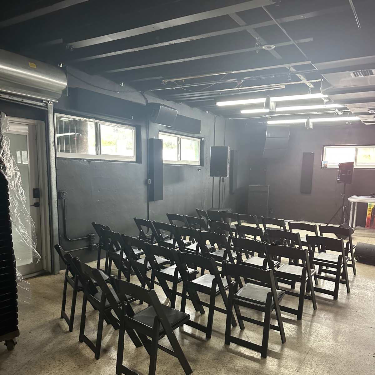 A room with several rows of black folding chairs set up facing a small stage area.