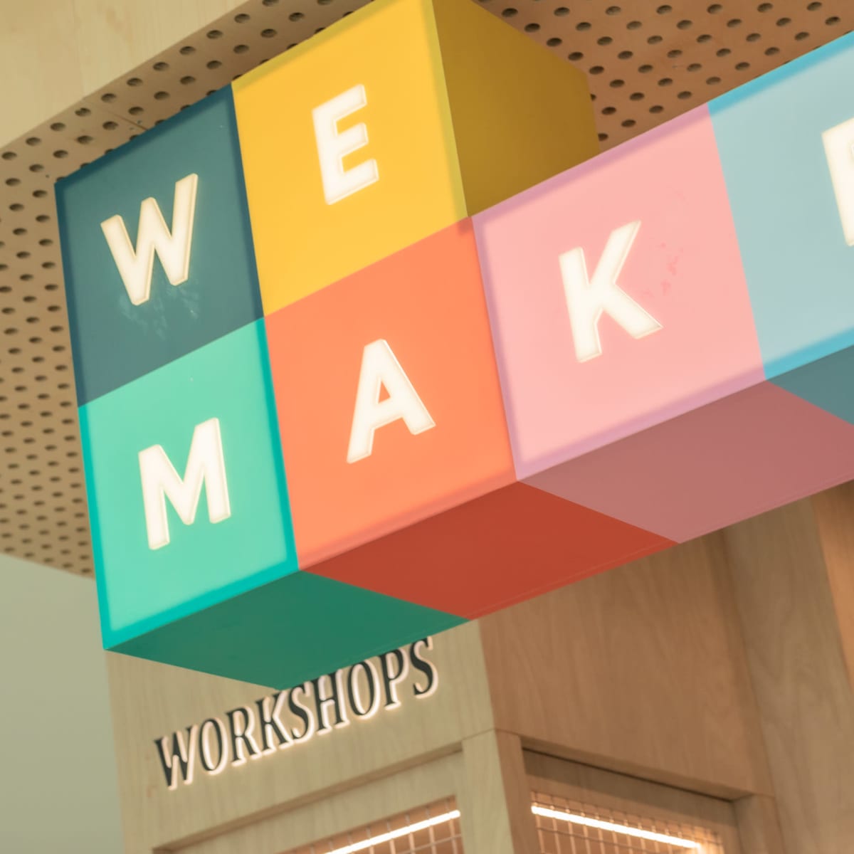 A colorful sign reading "WE MAKE" hangs above a wooden structure labeled "WORKSHOPS."