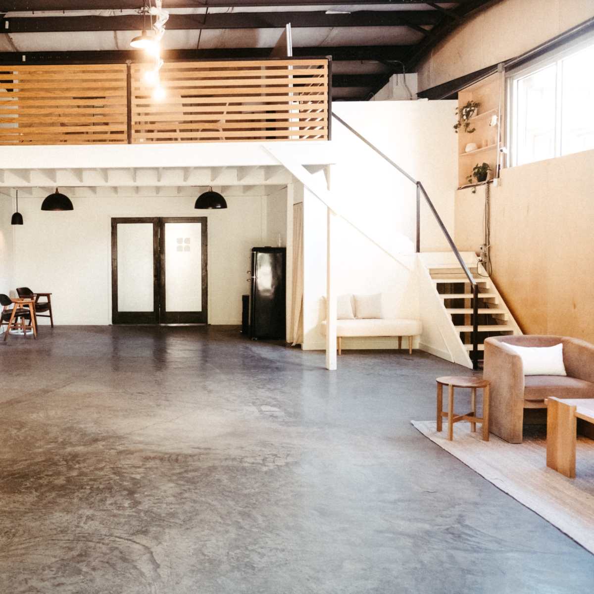 A spacious, minimalist interior with concrete flooring, a wooden mezzanine, and various seating options, including a sofa and chairs.