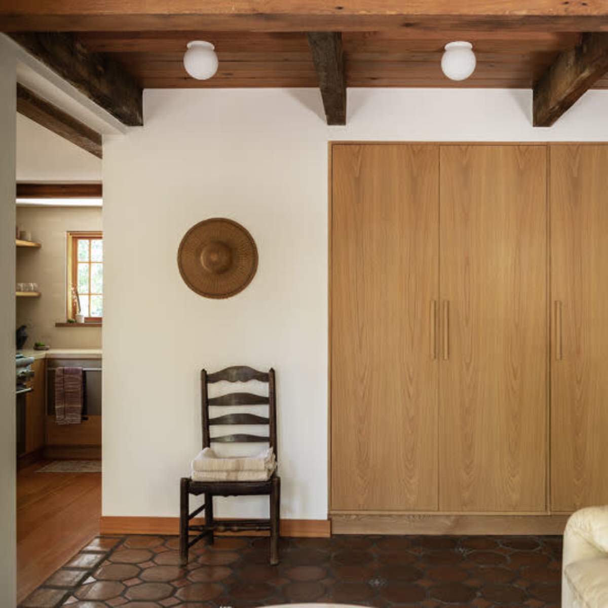 A simple interior space featuring a wooden closet, a single chair, and a view of a kitchen area beyond.