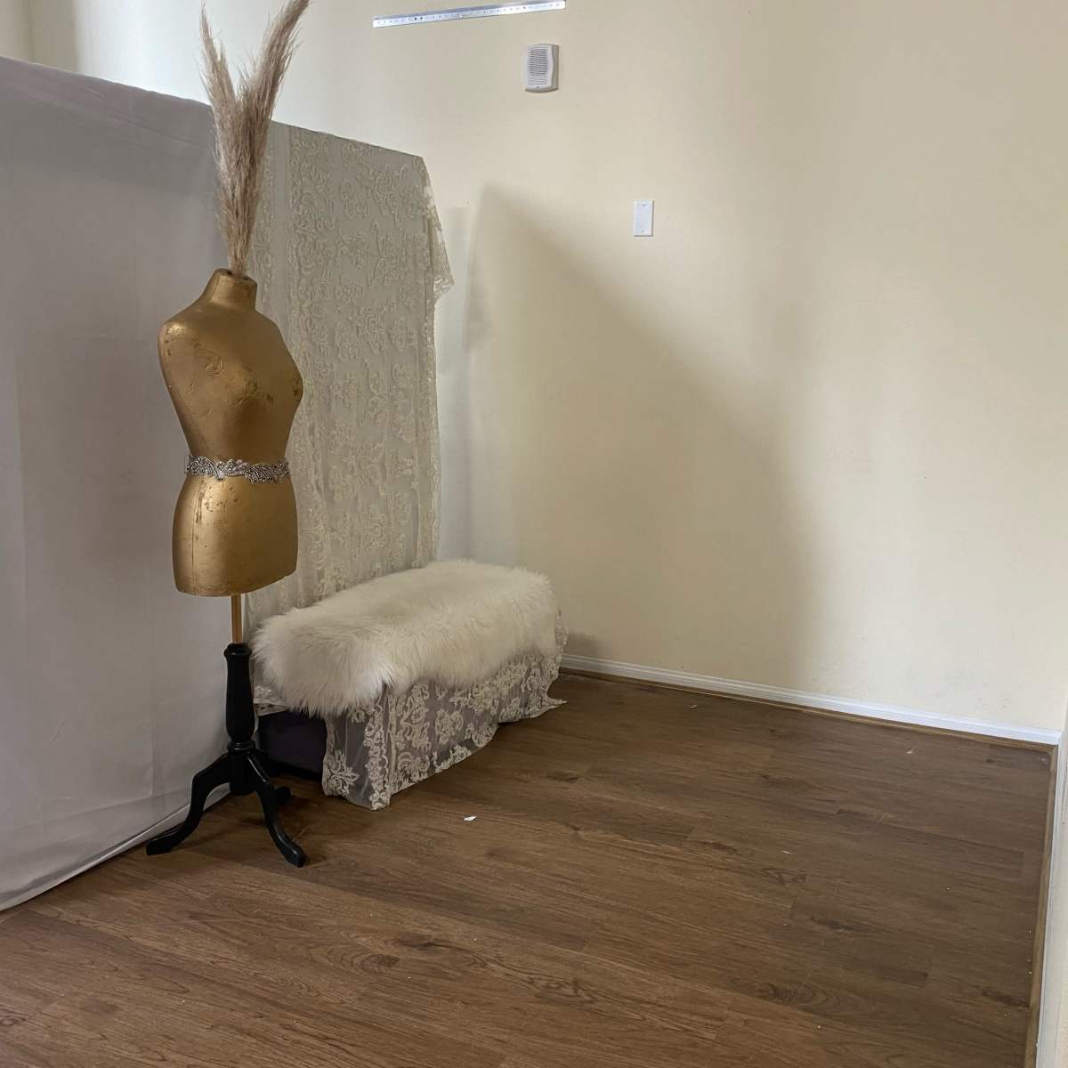An empty room featuring a gold dress form, a white fur bench, and a backdrop of fabric.