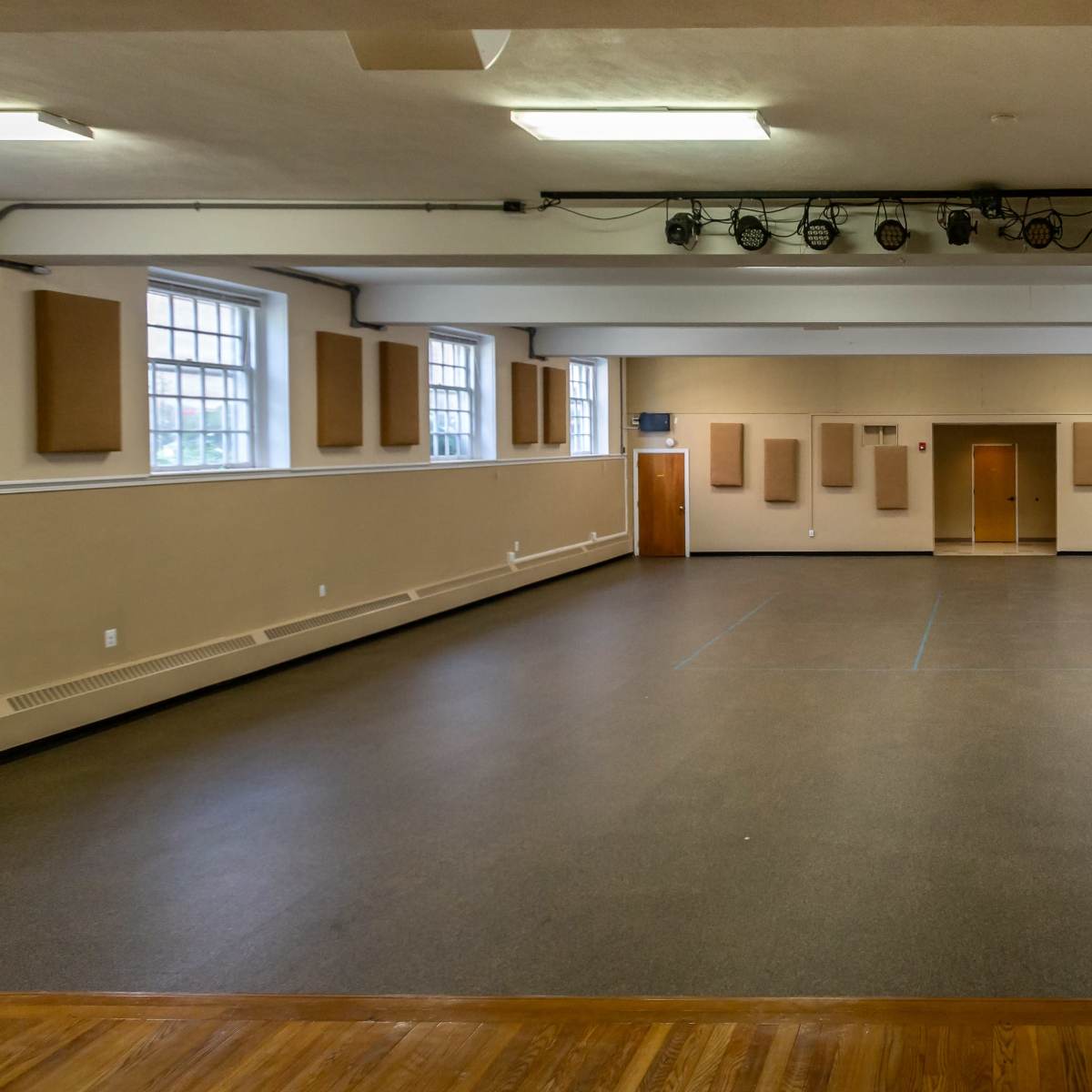 A spacious indoor hall with a polished wooden floor, beige walls, and sound-absorbing panels placed along the sides.