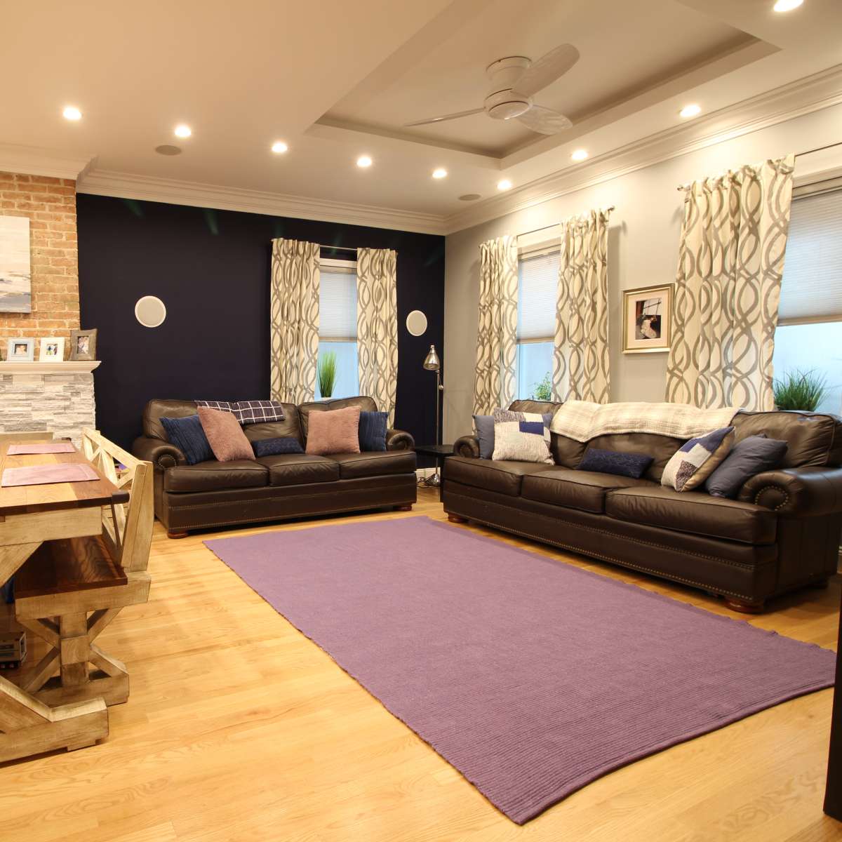 A living room features two leather sofas, a wooden dining table, and a fireplace with a brick accent wall.