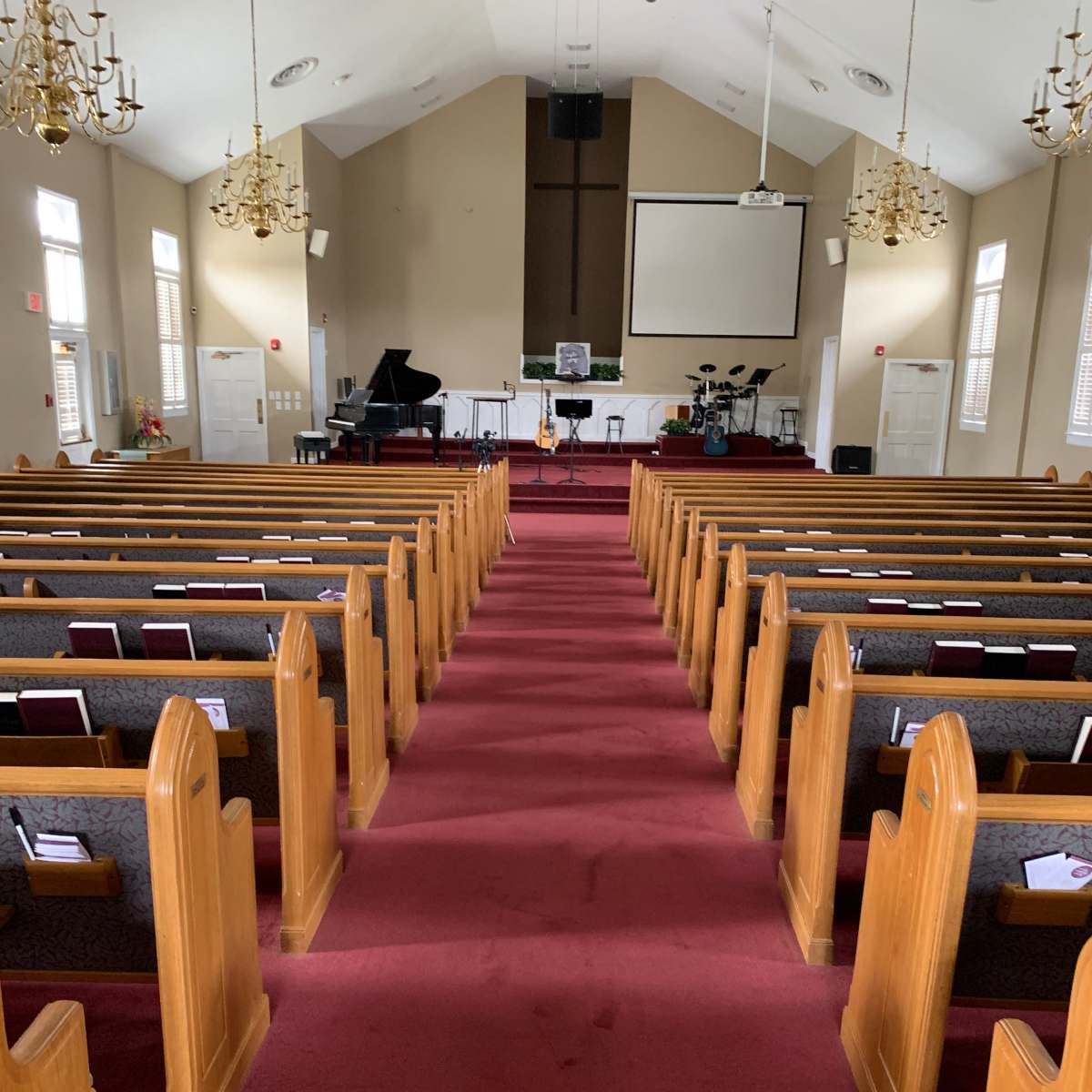 The interior of a church with wooden pews arranged in rows along a red carpet aisle leading to a stage with musical instruments.