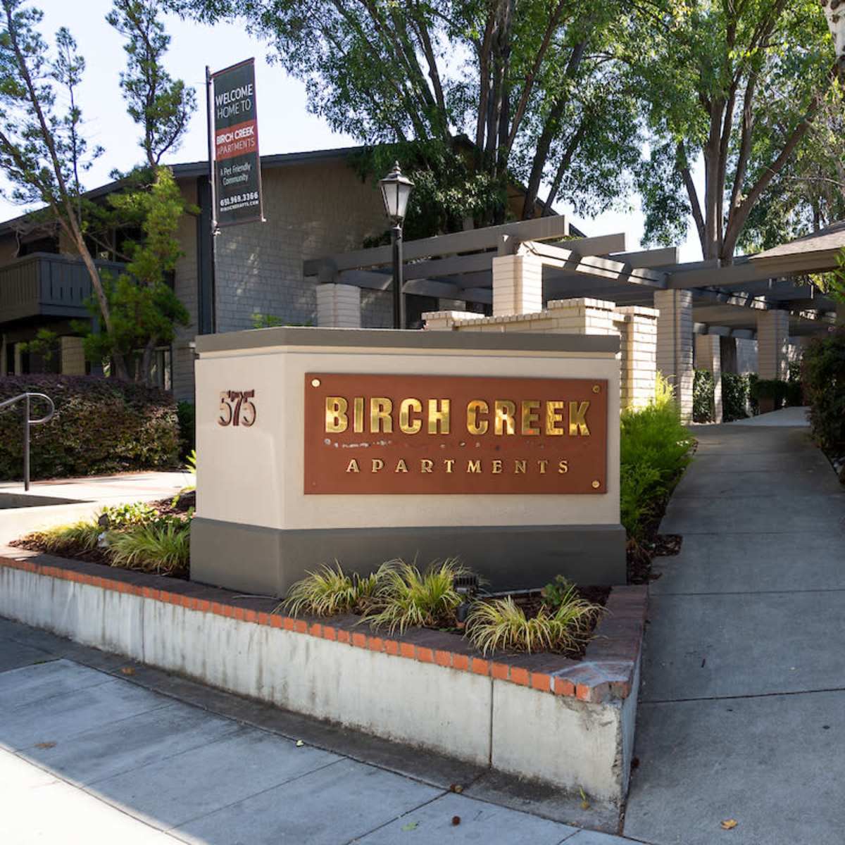 The entrance to Birch Creek Apartments features a sign and a landscaped pathway leading into the complex.