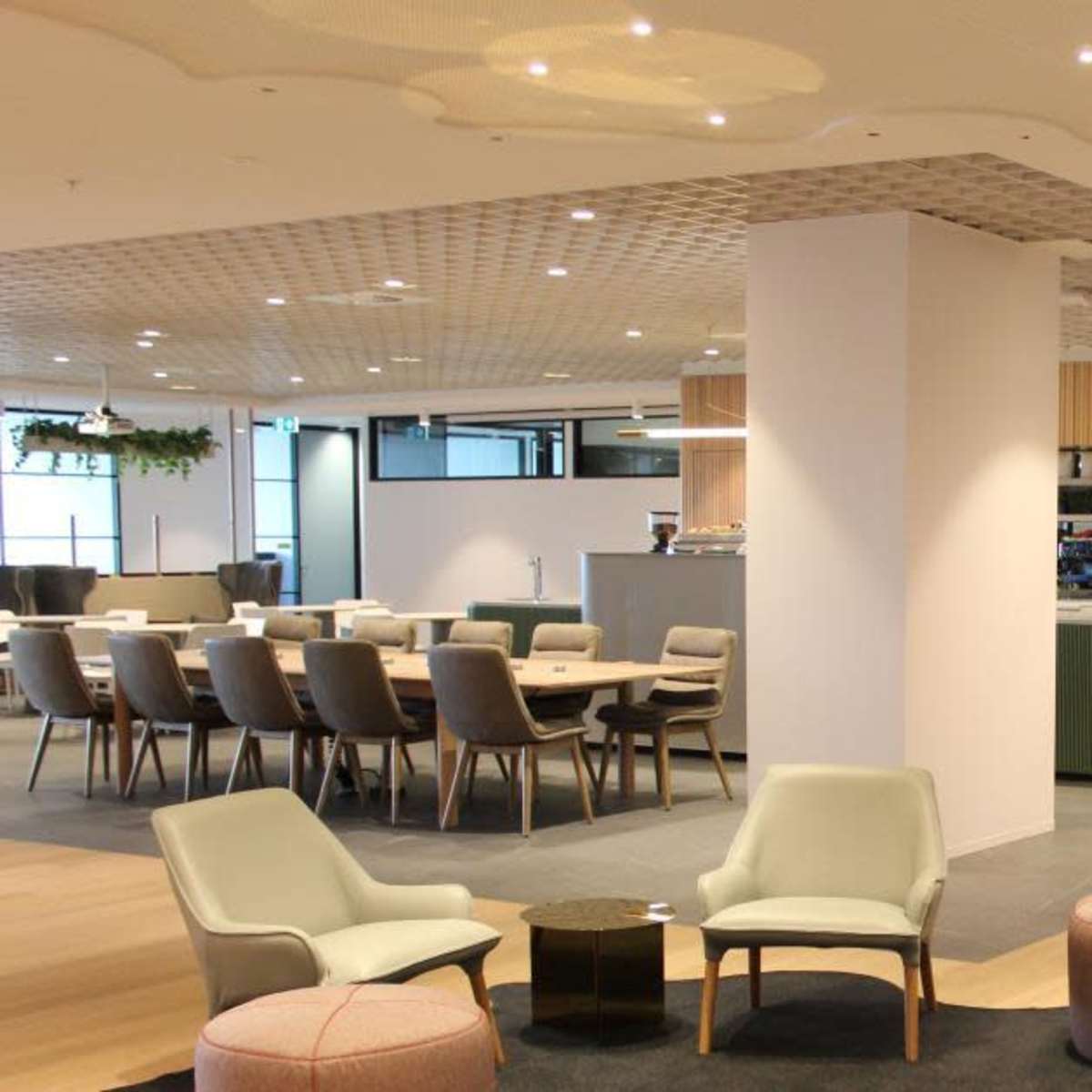 A modern office interior featuring a dining area with multiple seating arrangements, a coffee bar, and wooden accents on the walls.