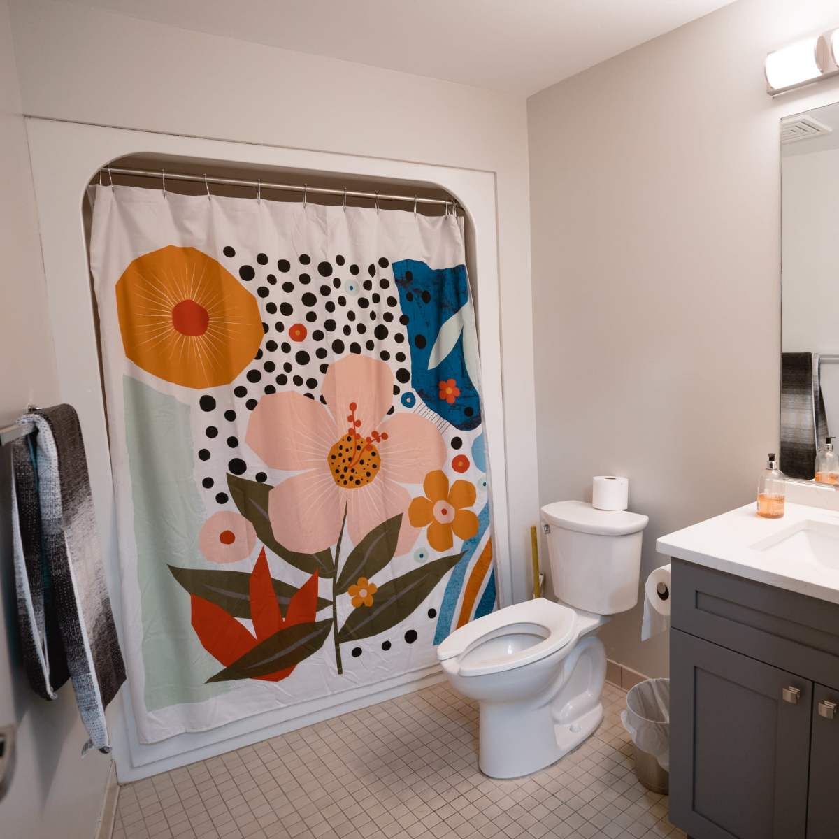 A modern bathroom featuring a colorful floral shower curtain, a sleek vanity with a sink, a toilet, and a large mirror with lighting above.