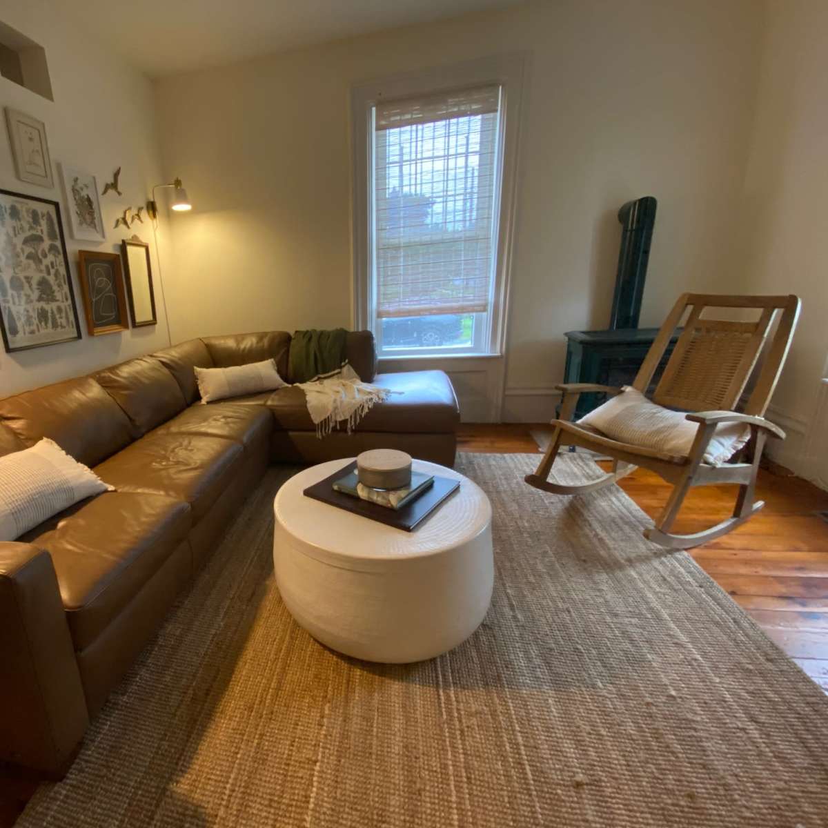 A living room with a brown sectional sofa, a round white coffee table, and a rocking chair, all arranged on a woven rug.