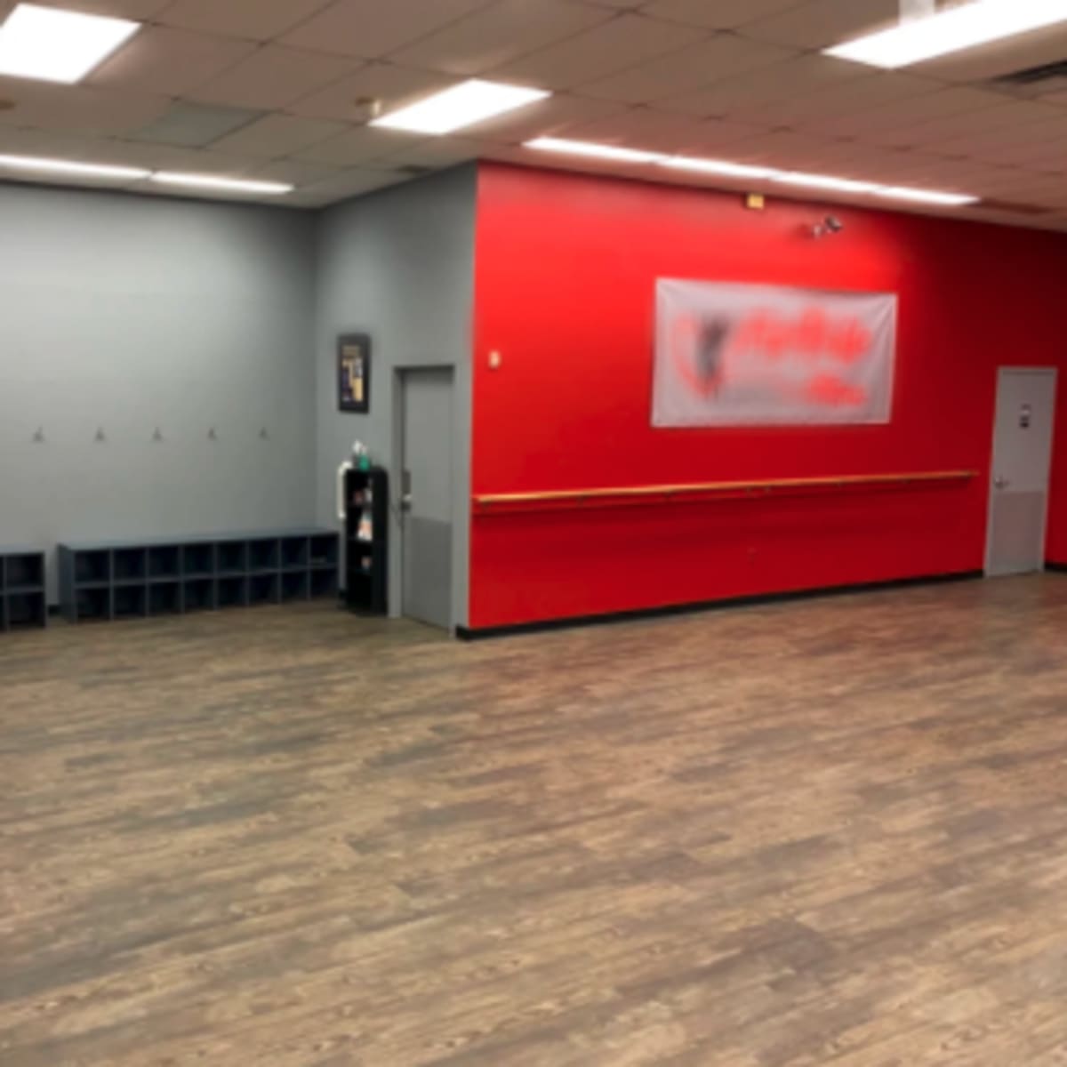 A spacious, empty room with red and gray walls, a wooden floor, and a row of hooks on one side.
