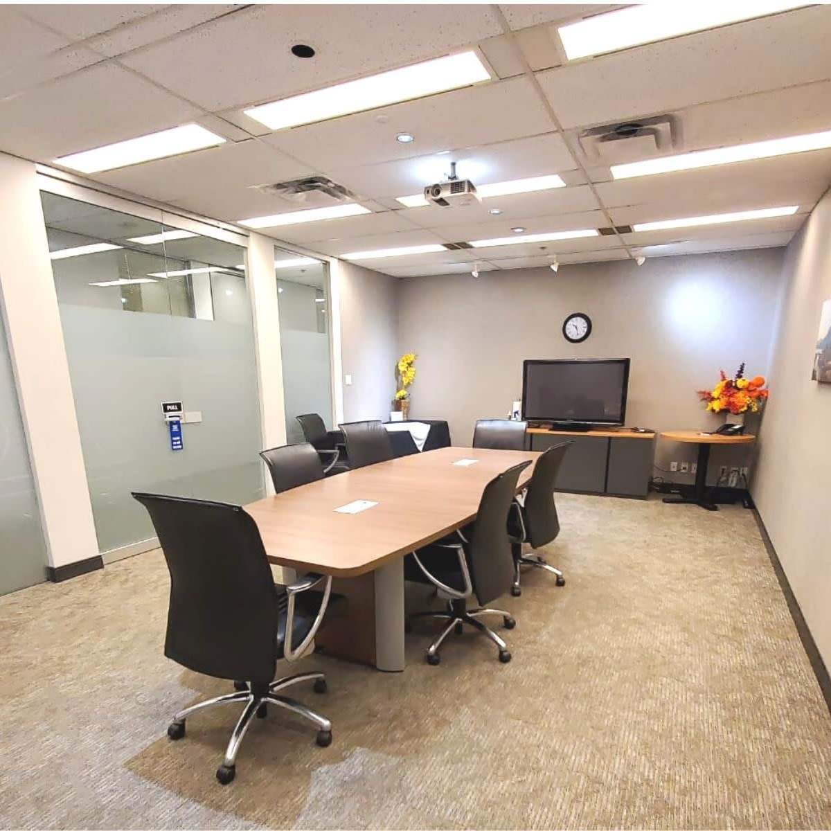 A modern conference room with a large table, ergonomic chairs, a television, and a wall clock.