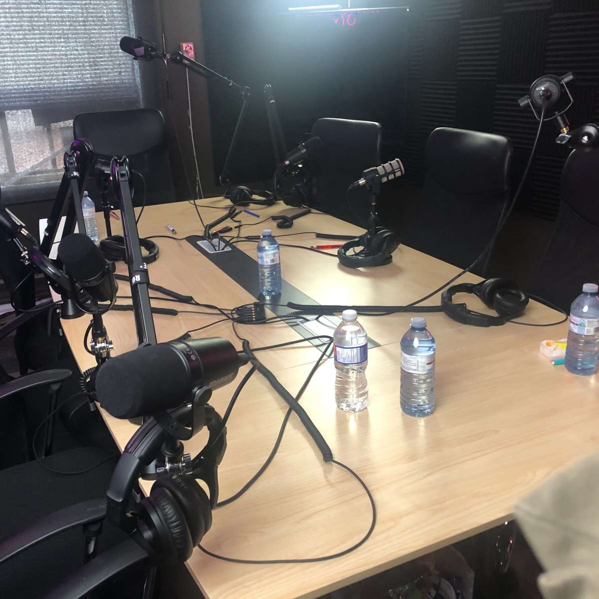 An empty podcast studio with chairs, microphones, and bottles of water arranged on a wooden table.
