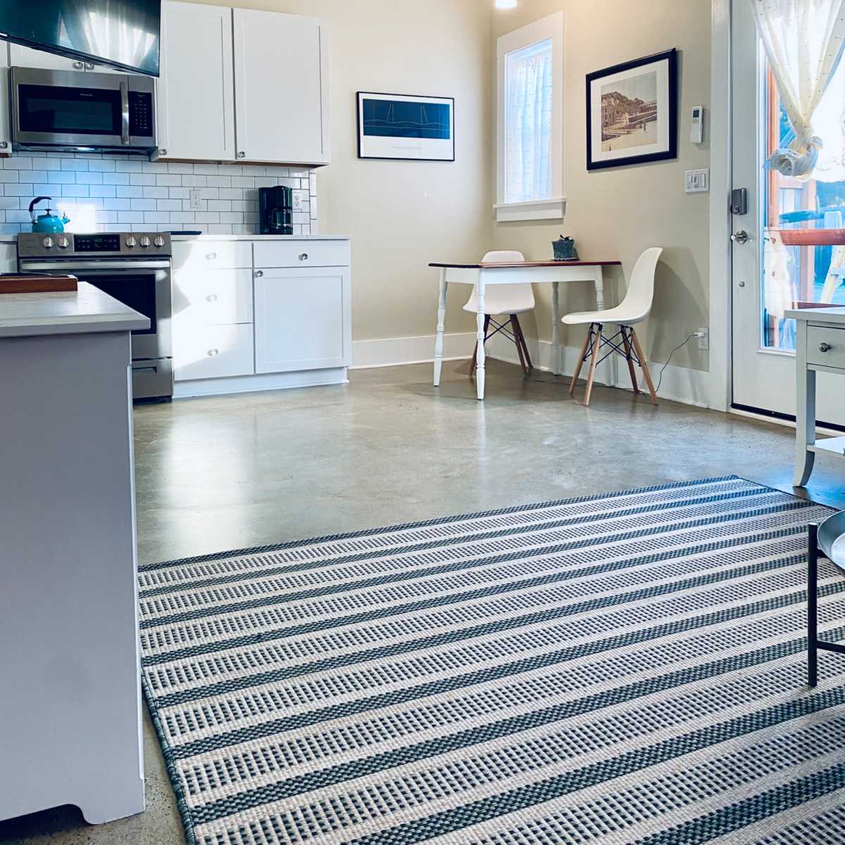 A modern kitchen with white cabinets, a stainless steel stove, and a small dining table beside a door leading outside.