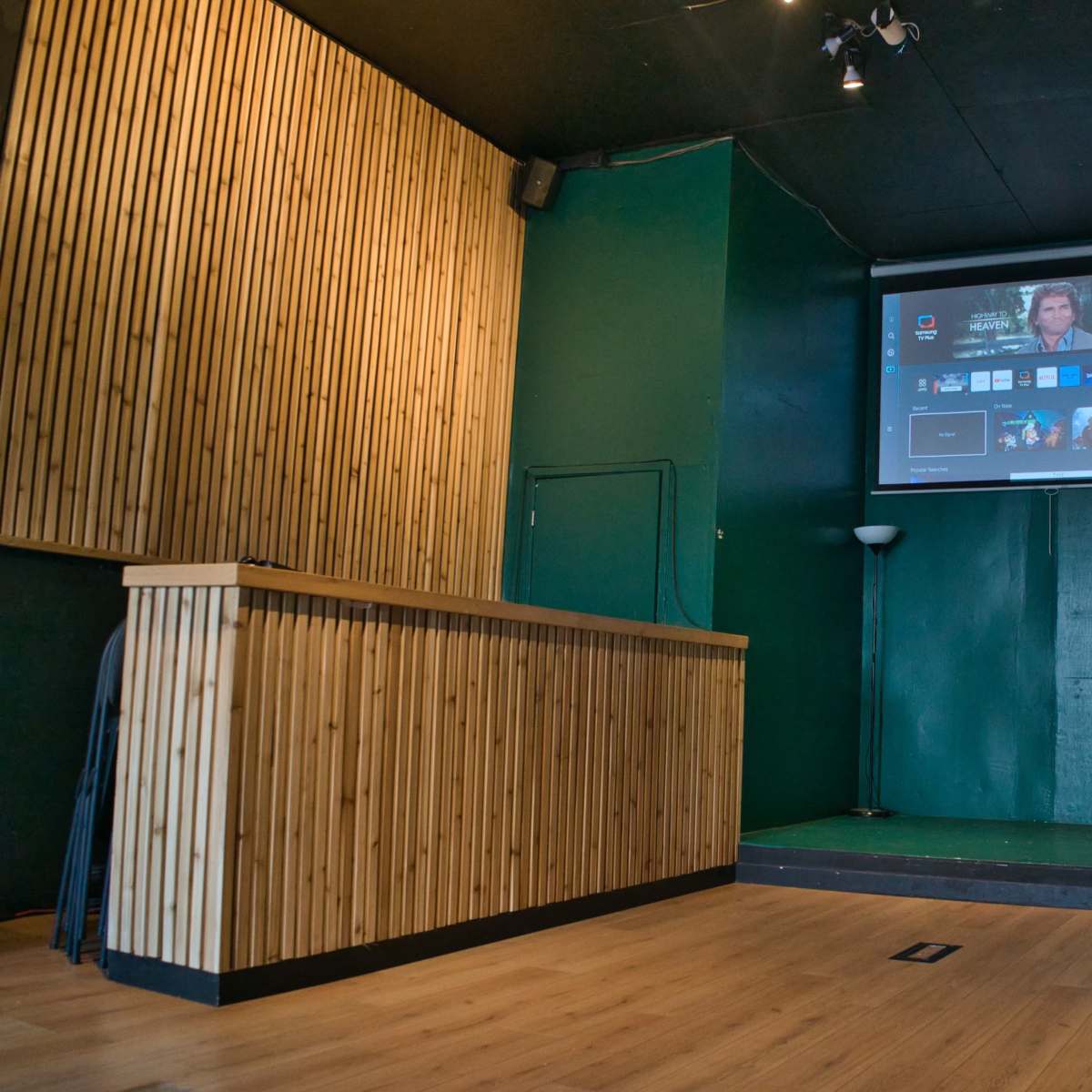 A green-walled room with a wooden reception counter, a large screen displaying content, and a stage area in front.